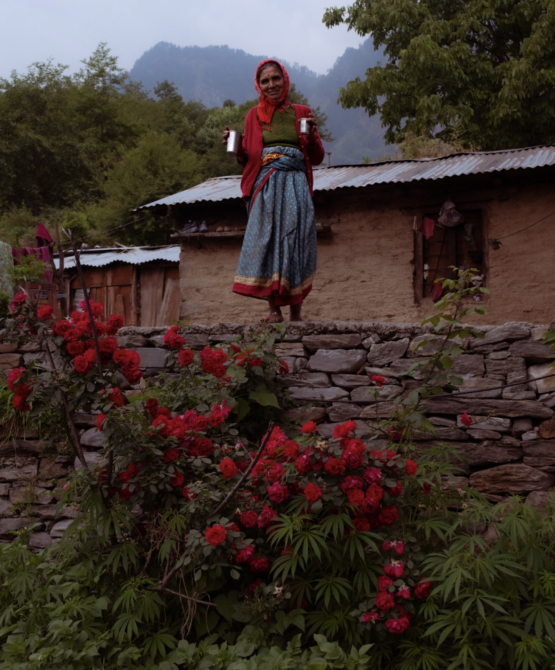 Woman standing above a wall of red roses by her village home
