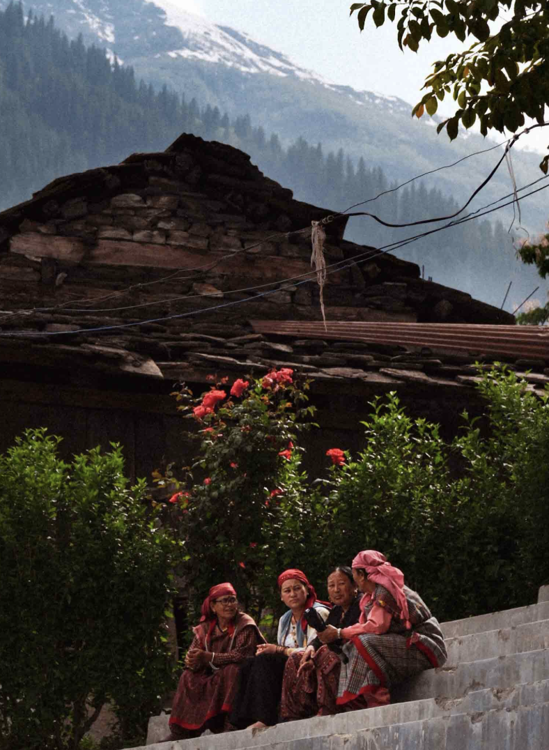 Four women sitting together on stone steps with mountains behind